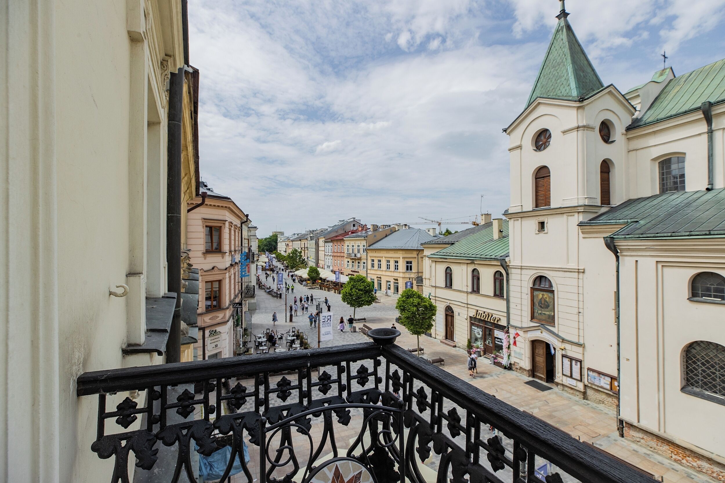 A balcony with a wrought iron railing overlooking a street with historic buildings and a church.