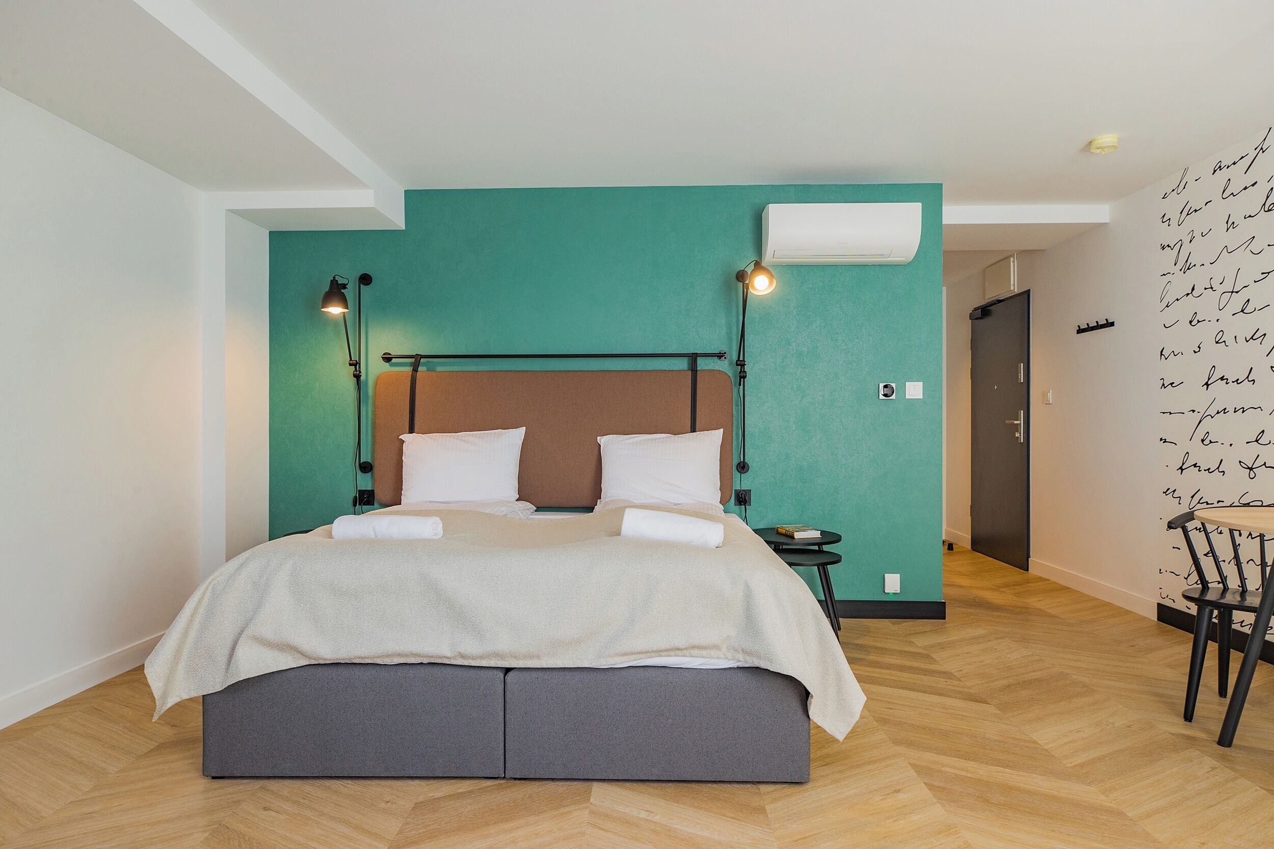Quarto moderno com cama, abajures, uma mesinha e uma cadeira.