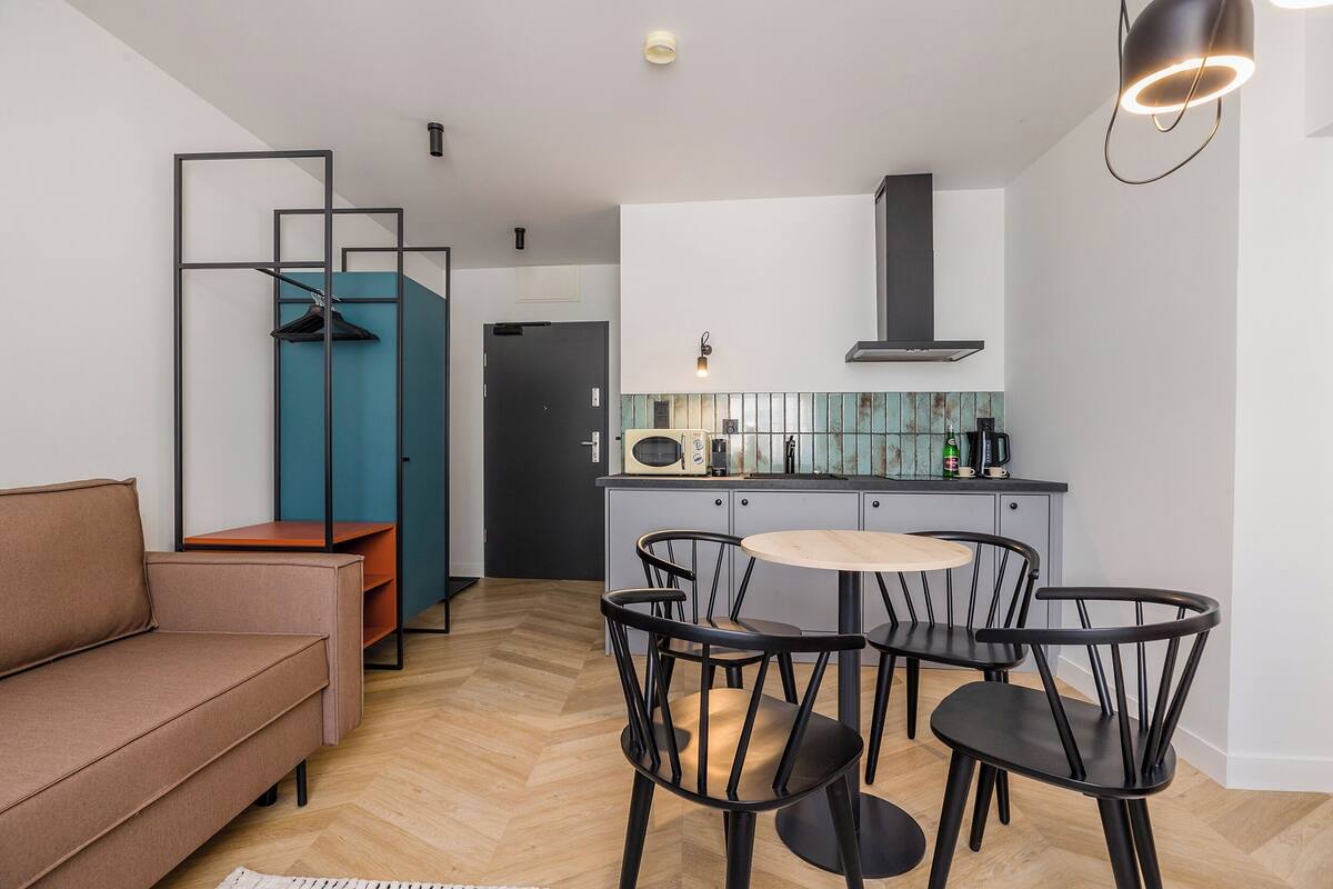 A modern kitchen with a central island, black chairs, and a grey sofa.