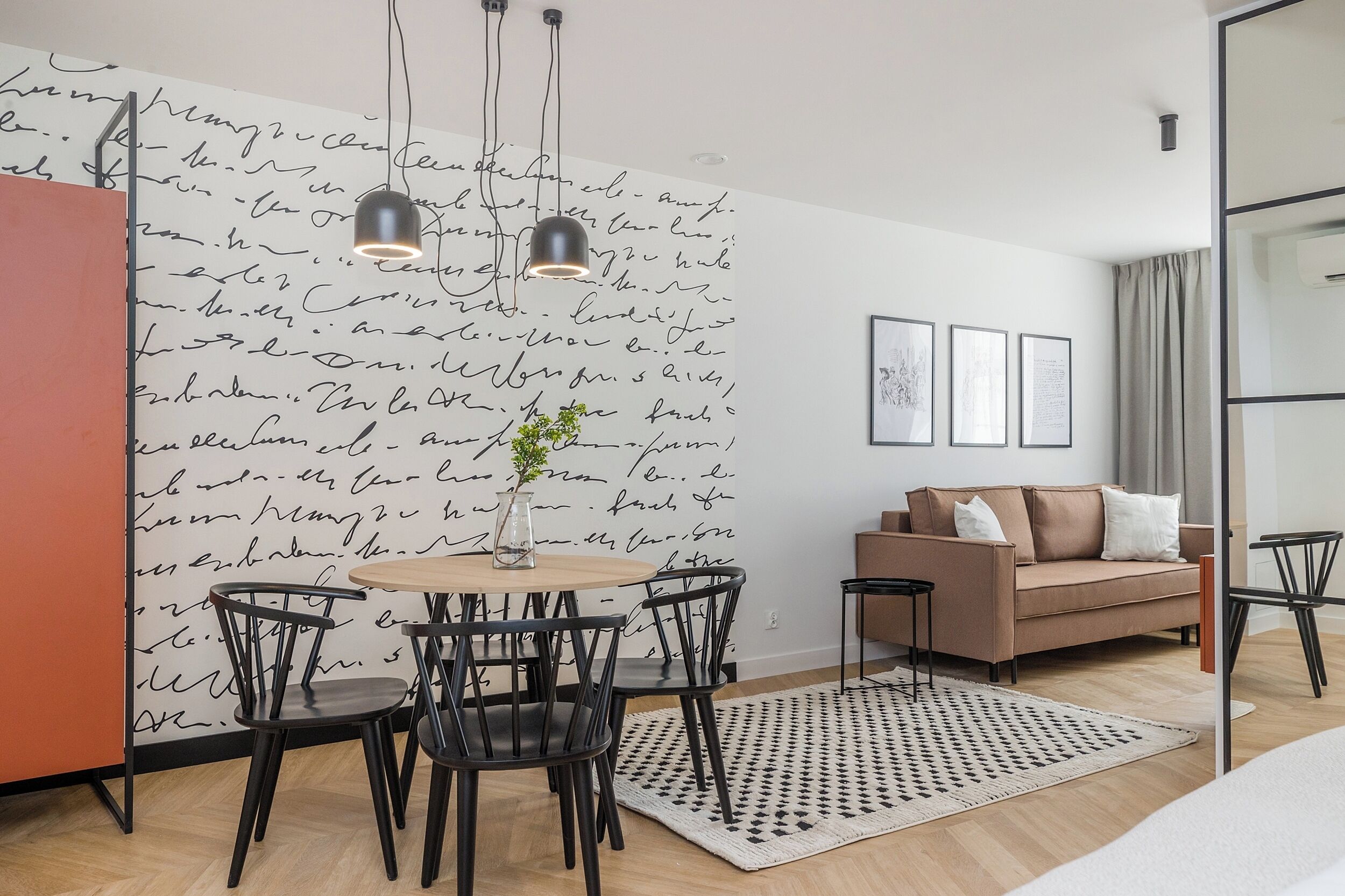 Un salon moderne avec une table ronde en bois, des chaises noires, un canapé beige et un tapis à motifs.