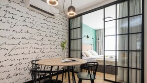 Une chambre moderne dotée d’une grande fenêtre, d’un lit, d’une table avec des chaises et d’un mur sur lequel est écrit un texte manuscrit.