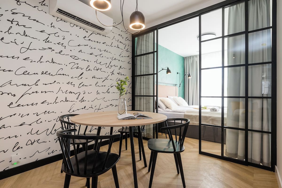 A modern room with a large window, a bed, a table with chairs, and a wall with handwritten text.
