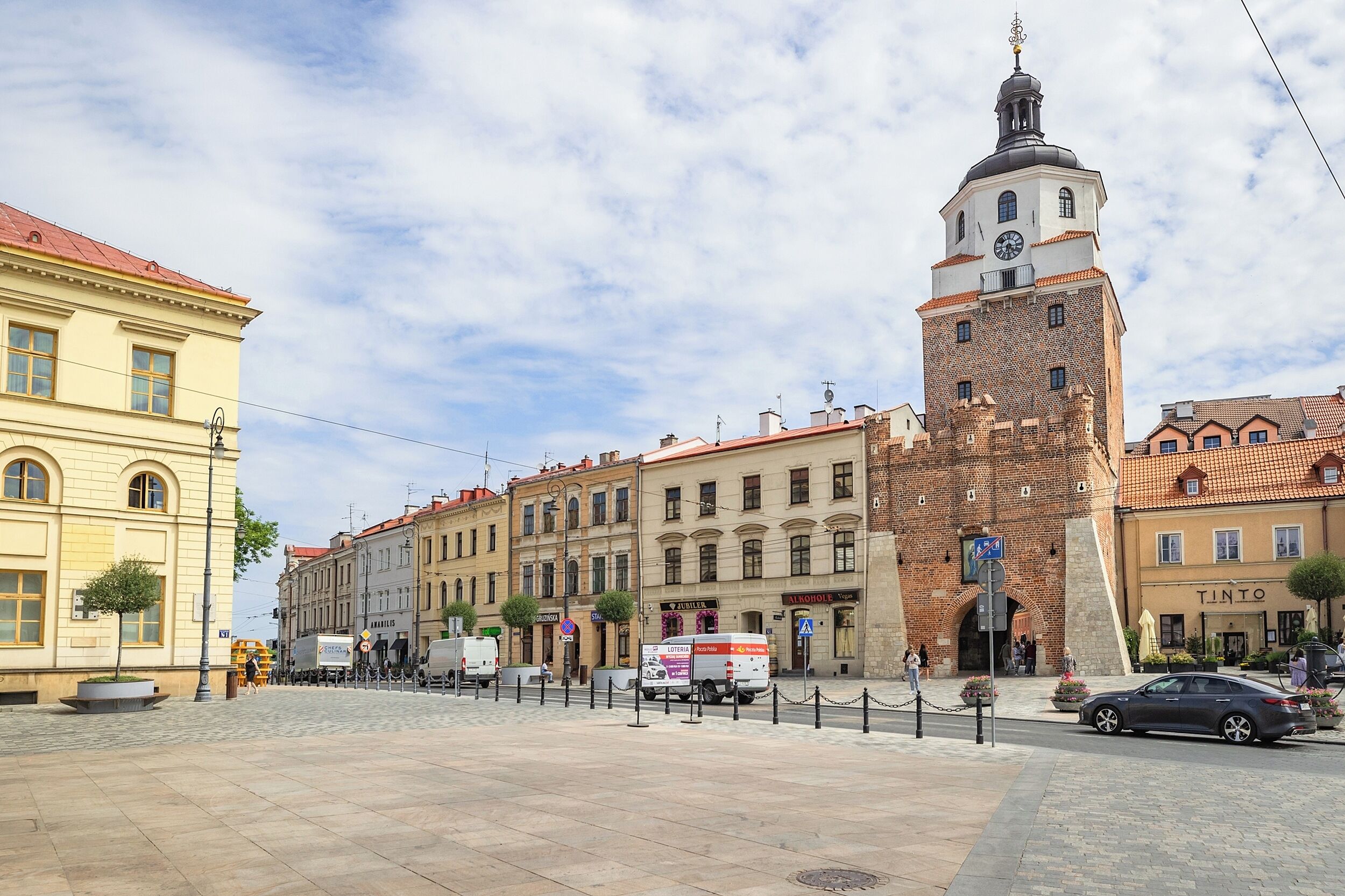 Un edificio histórico con una torre de reloj, rodeado de otros edificios con comercios.