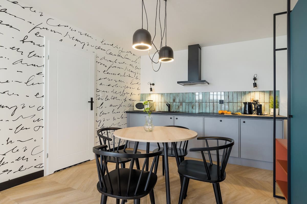 A modern kitchen with a round wooden table and black chairs, a white door with handwritten notes, and pendant lighting.