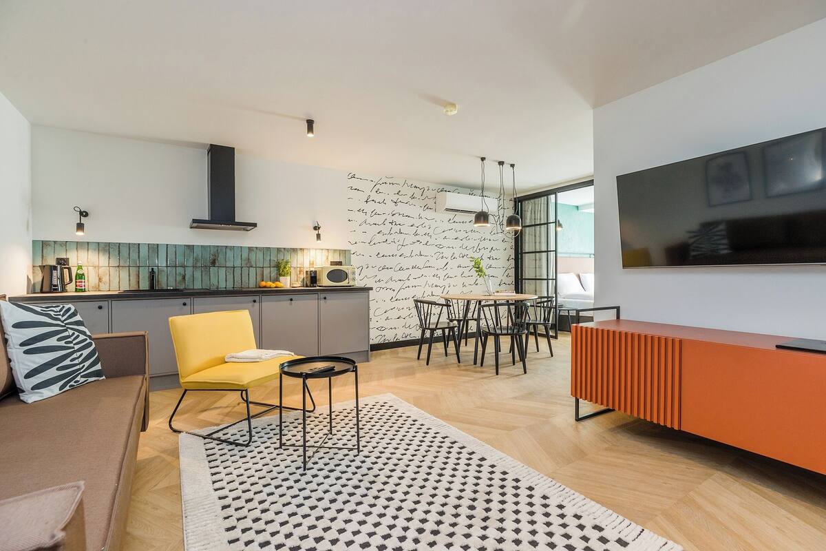 A modern kitchen with a dining area, a sofa, and a TV.