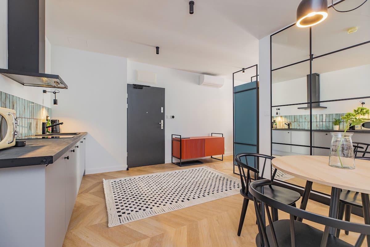 A modern kitchen with a wooden herringbone floor, a central island with a sink, and a dining area with a round table and chairs.