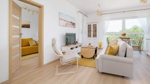 A modern living room with a sofa, a chair, a TV, and a dining area with a table and chairs. - Bright Apartment with a Balcony | Lake View, Bicycles (Katowice)
