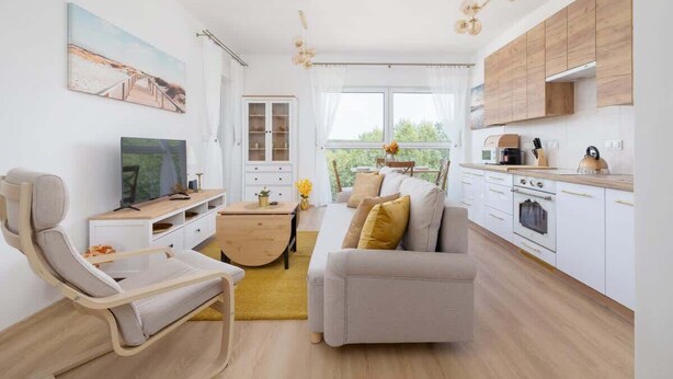 A modern living room with a sofa, a TV, and a dining area with a table and chairs. - Bright Apartment with a Balcony | Lake View, Bicycles (Katowice)