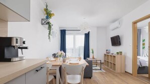 Een moderne keuken met een koffieapparaat, eettafel en stoelen. Er is een televisie aan de muur bevestigd en een raam met gordijnen.