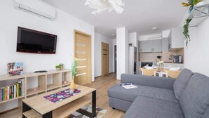 Een moderne woonkamer met een grijze bank, een houten salontafel en een televisie aan de muur. Er staat een boekenkast met boeken en een klein plantje ernaast.
