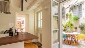 Une cuisine moderne avec un plan de travail en bois, un coin repas avec une table ronde et des chaises colorées, et une vue sur un jardin par une porte ouverte.