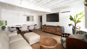 Un salon moderne comprenant un canapé, une table à manger, des chaises, un téléviseur et une plante.