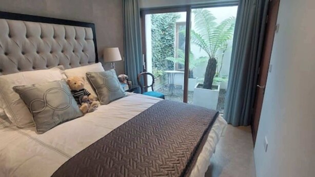 Ein Schlafzimmer mit einem großen Bett, einem Kopfteil und Blick auf einen Balkon mit Pflanzen.