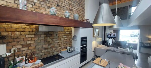 Una cocina moderna con pared de ladrillo, estante de madera e iluminación colgante.