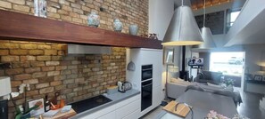 Eine moderne Küche mit Backsteinwand, Holzregal und Pendelleuchten.
