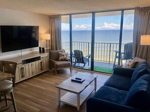 Ein Wohnzimmer mit großem Fernseher, einer Couch, einem Couchtisch und Meerblick durch große Fenster.