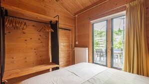 Puisesta materiaalista tehty huone, jossa on sänky, puinen penkki ja ikkuna, josta on näkymä ulos.
