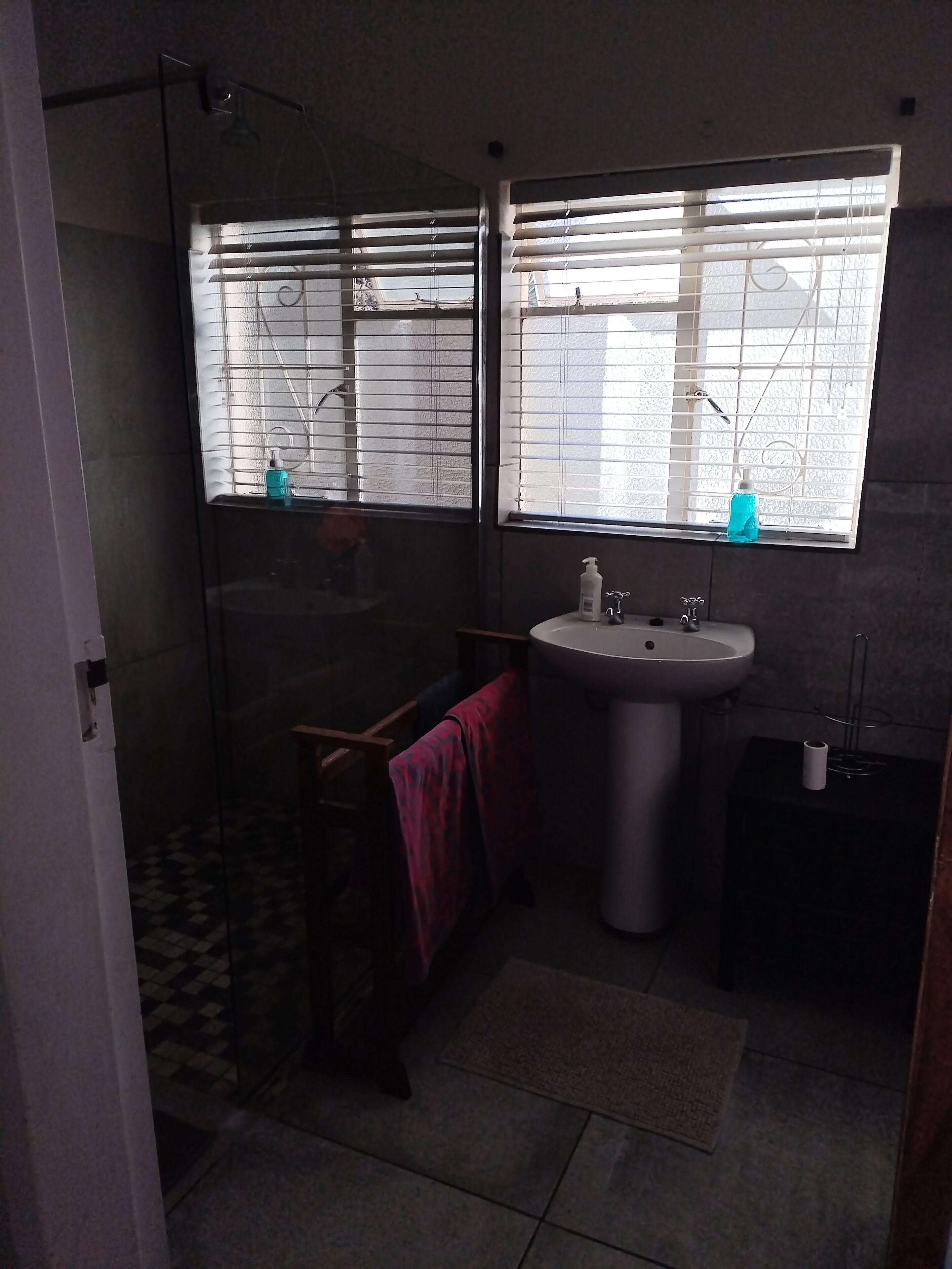 Un baño con cabina de ducha de vidrio, un lavabo con espejo y una ventana con persianas.