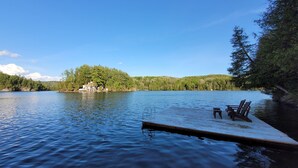 Une jetée au bord du lac, avec deux chaises Adirondack, une plateforme en bois s’étendant dans une eau calme, et une île boisée en arrière-plan.