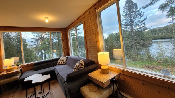 L'intérieur d'un chalet chaleureux, avec une grande fenêtre donnant sur une forêt et un lac.