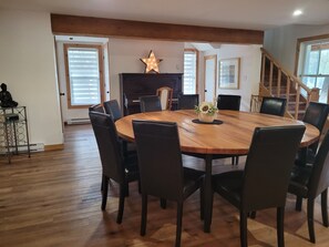 A dining area with a round wooden table surrounded by chairs, a star-shaped light fixture above the table, and a staircase in the background.