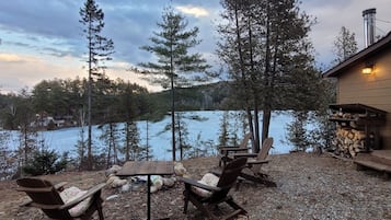 Relax in a serene lakeside setting with a comfortable seating area featuring a wooden table and two Adirondack chairs.