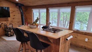 A wooden cabin kitchen with a central island, two black chairs, a sink, and a stove.