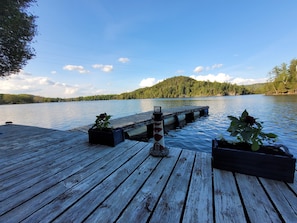 A wooden dock extending into a calm lake, surrounded by lush greenery and a forested hill in the background. - Intimate Cottage plus Loft with Epic Lake Views (Val-des-Monts)
