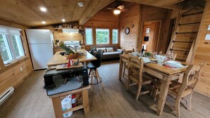 A cozy cabin-style kitchen with wooden walls and floors, a dining table set for four, and a refrigerator in the corner.