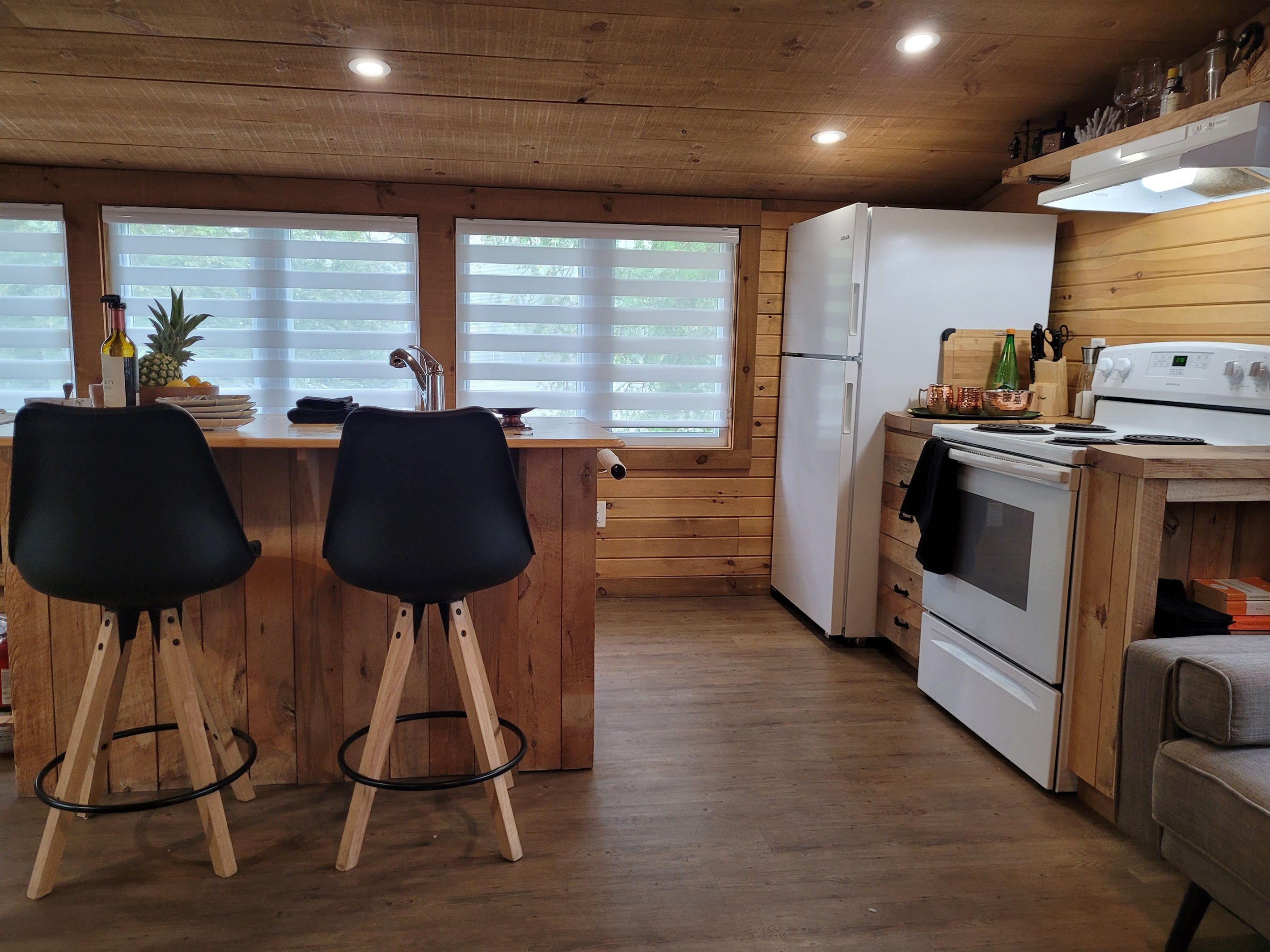 A kitchen with wooden cabinets, a white refrigerator, a stove, and two black bar stools.