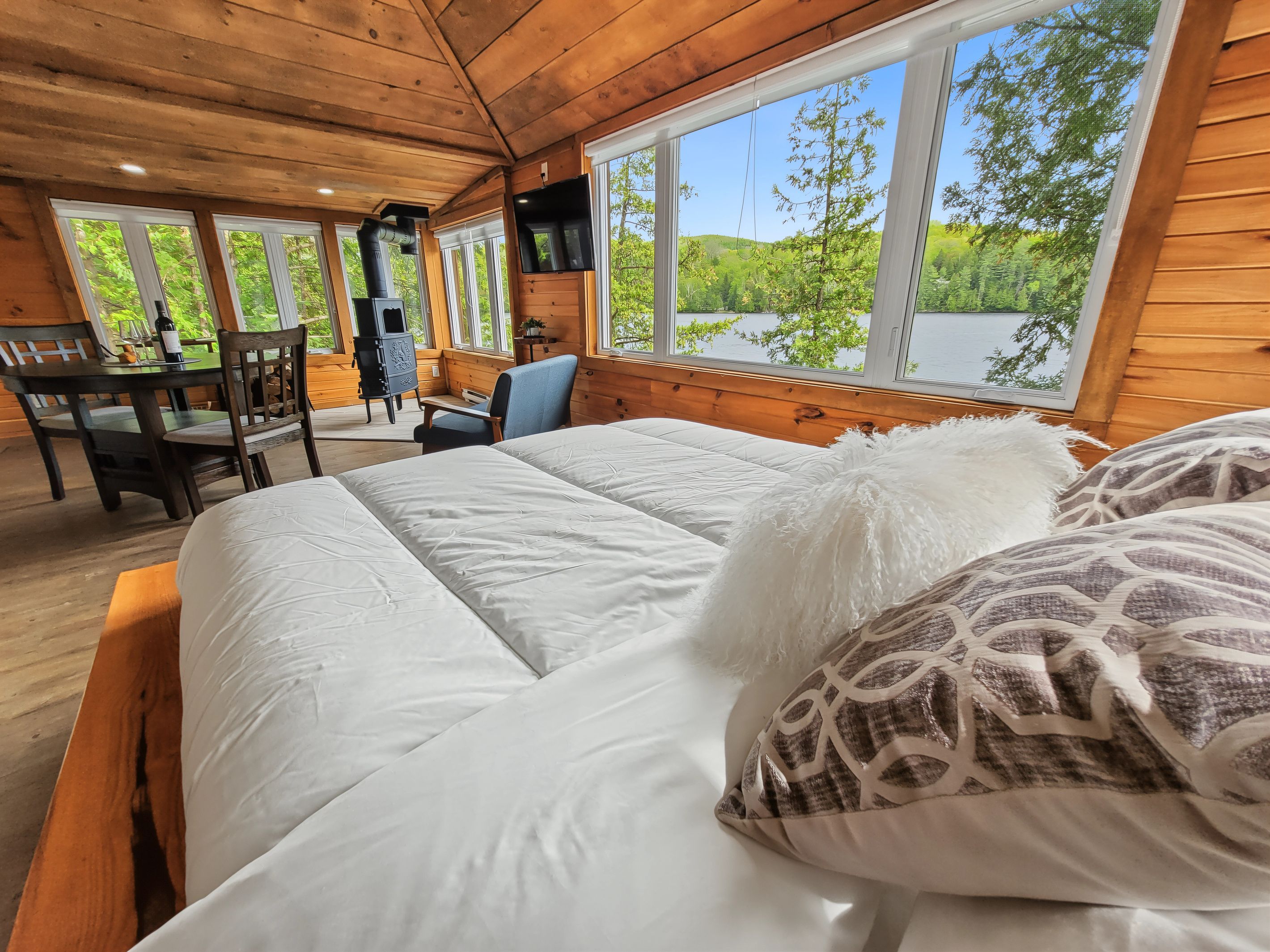 A wooden cabin room with a large bed, a desk, and a television.