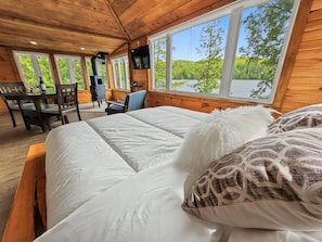 A wooden cabin room with a large bed, a desk, and a television. - Romantic Cottage with Epic Lake Views (Val-des-Monts)
