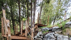 A wooden staircase leading up to a wooden platform, surrounded by rocks and trees.