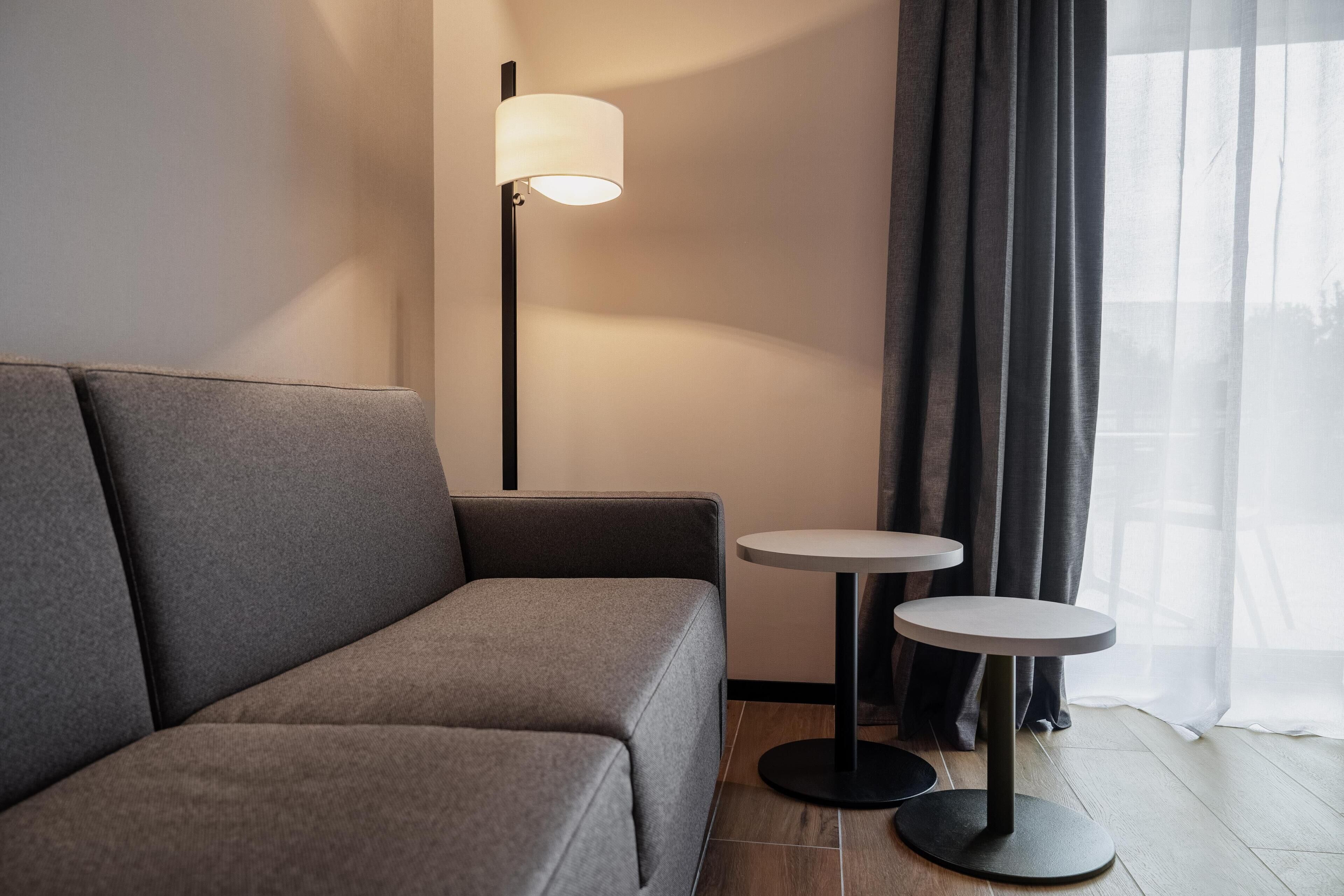A modern room with a grey sofa, two small round tables, and a floor lamp.