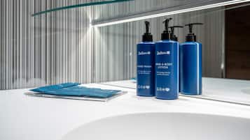 A bathroom with a glass shelf holding three blue bottles of Radisson hand wash and body lotion, and a blue tissue box on the counter.