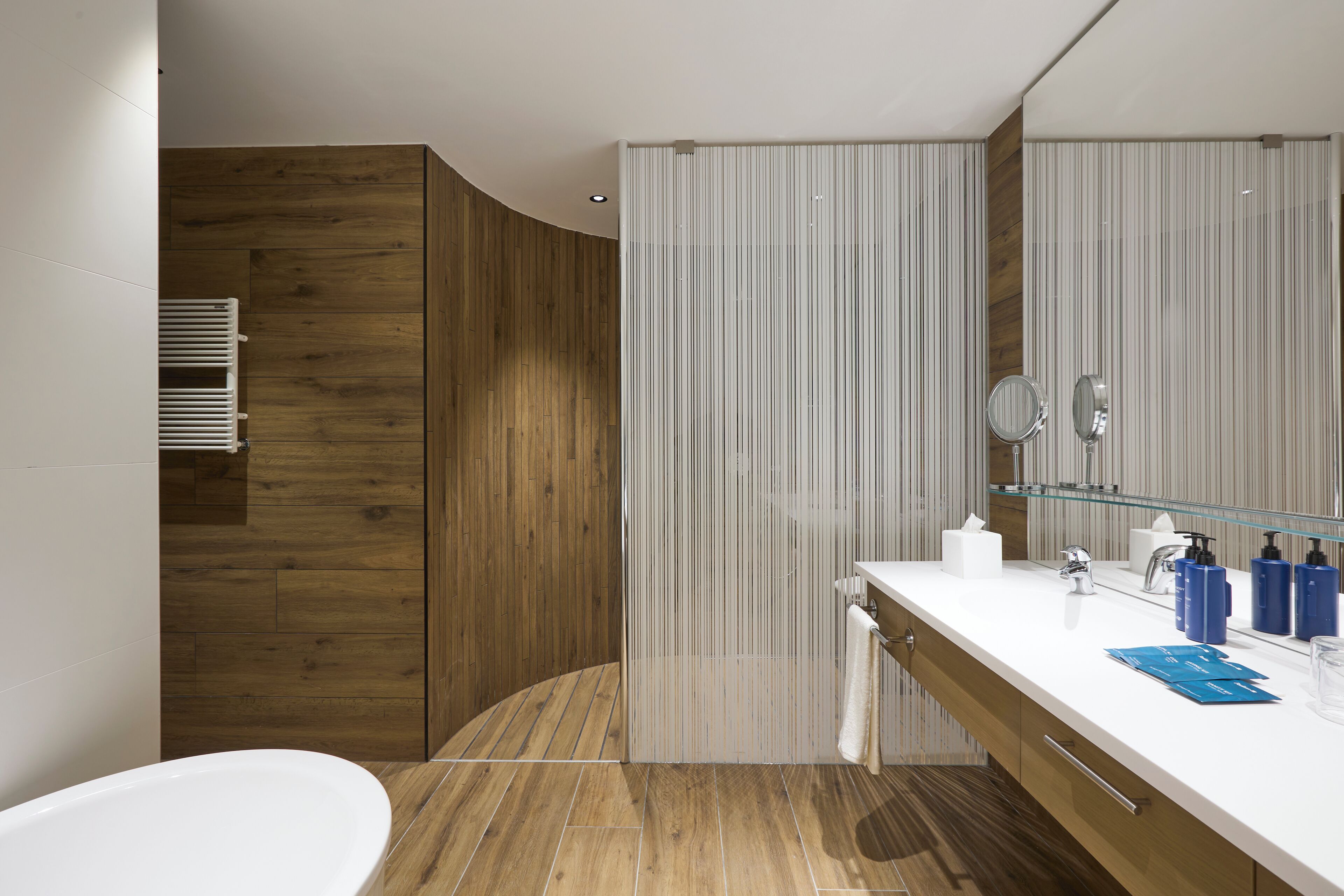 A modern bathroom with a wooden vanity, a large mirror, and a white bathtub.