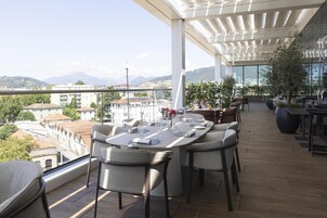 Zona pranzo sul tetto con tavolo imbandito per quattro, con vista su un panorama urbano e montagne sullo sfondo.