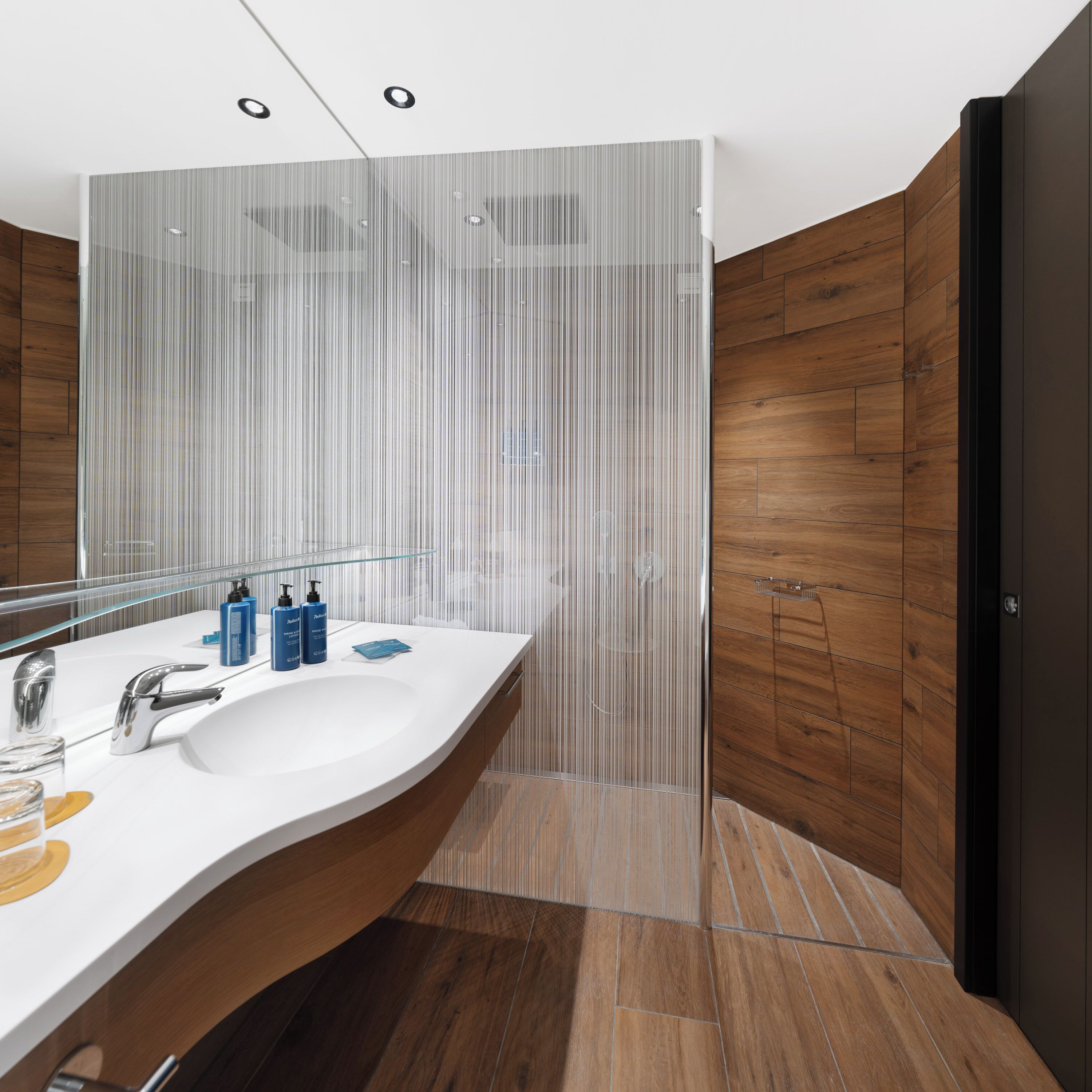 Une salle de bain moderne avec un meuble-lavabo aux lignes courbes, un grand miroir et un lambris en bois.