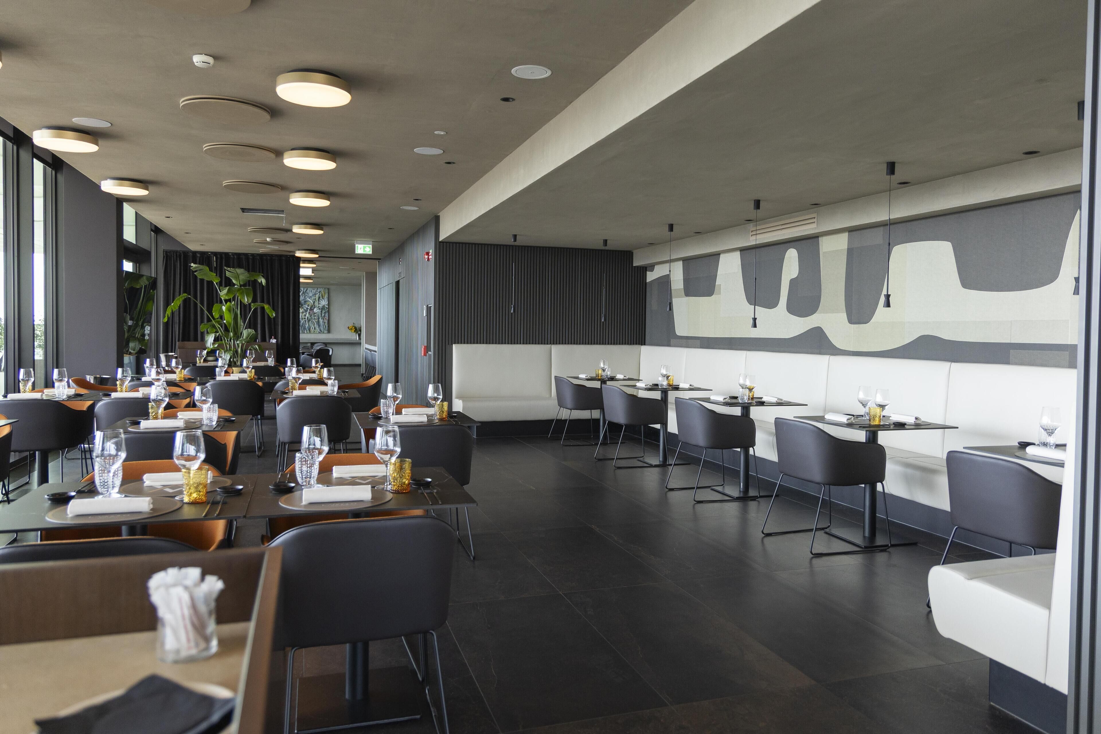 A modern restaurant with a long counter, multiple tables, and chairs.