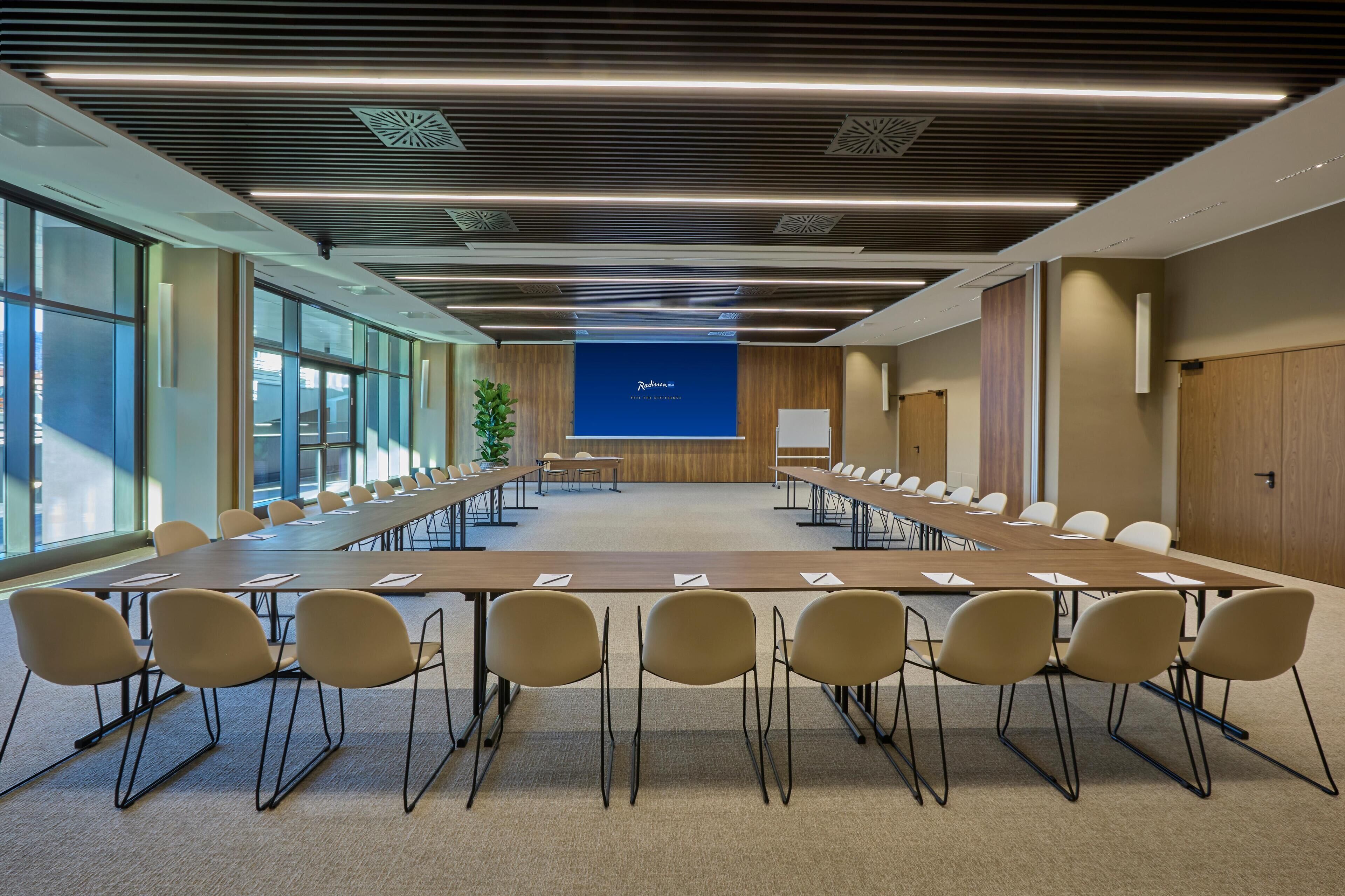 A conference room with a long table, chairs, a projector screen, and a plant.