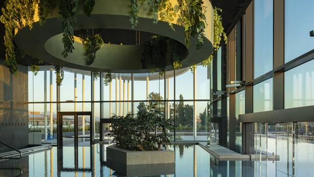 Een modern binnenzwembad met glazen wanden, een plantenbak met beplanting in het midden en een rond dakontwerp.
