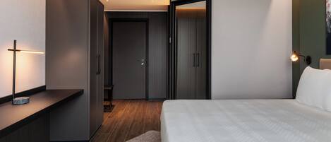 A modern hotel room with a large bed, a desk, and a wardrobe.