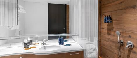 A modern bathroom with a wooden wall, a glass shower enclosure, and a white sink with toiletries.