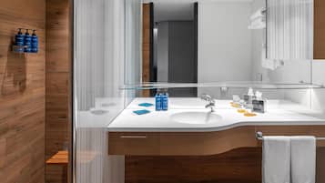 Un bany modern amb una paret de fusta, una cabina de dutxa de vidre i un lavabo blanc amb productes de tocador.