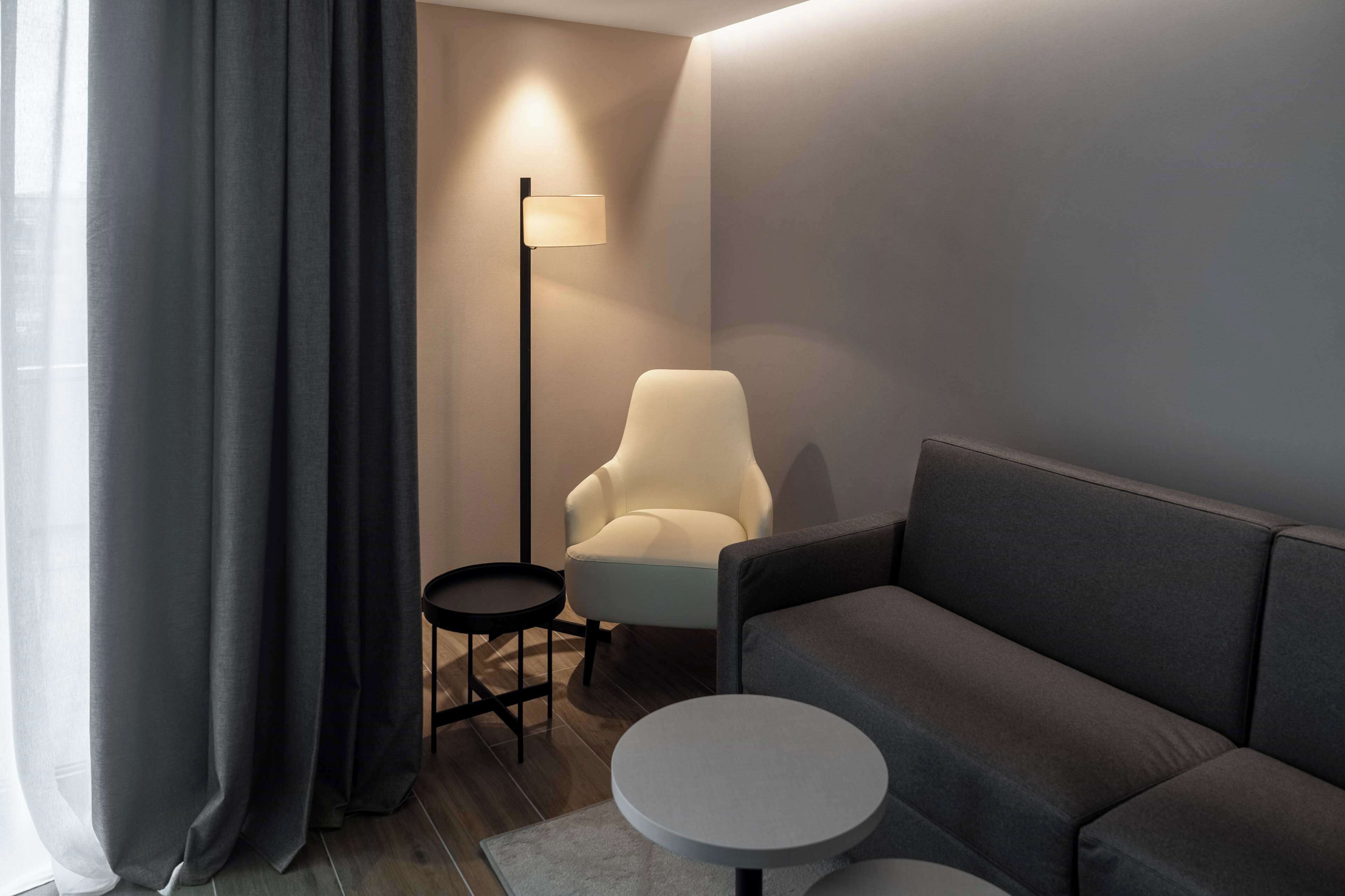 A modern living room with a grey sofa, a small round table, a white armchair, and a floor lamp.