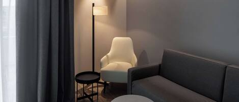 A modern living room with a grey sofa, a small round table, a white armchair, and a floor lamp.