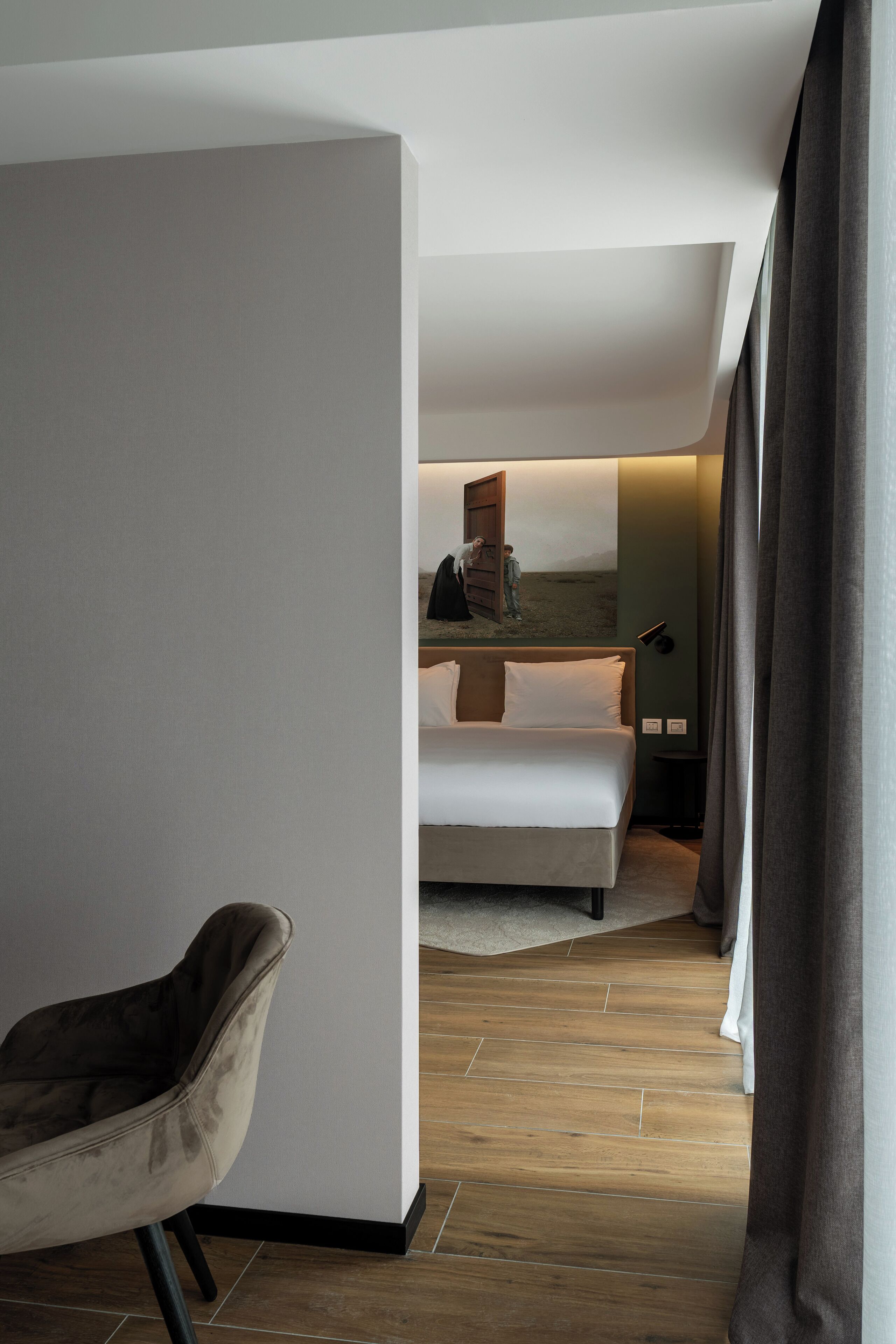 A modern hotel room with a bed, a chair, and a painting on the wall.