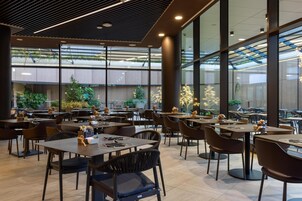 Un ristorante moderno con ampie vetrate, piante interne e diverse tipologie di posti a sedere.