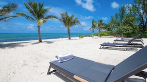 A beach with white sand, palm trees, and lounge chairs.