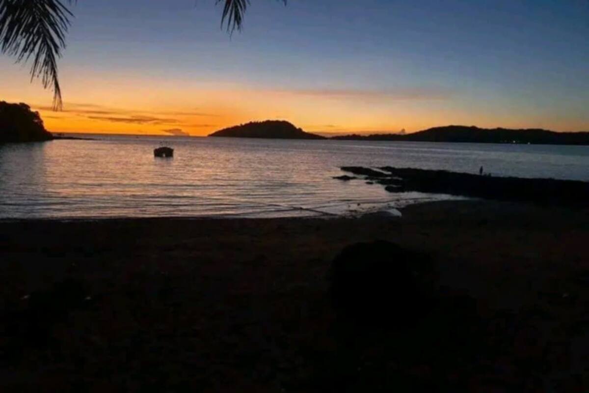 A beach at sunset with calm waters and distant hills.